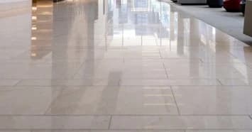 Ein glänzender Marmorboden reflektiert das Licht und die Architektur eines modernen Gebäudes. Die polierte Oberfläche erzeugt ein spiegelähnliches Bild.